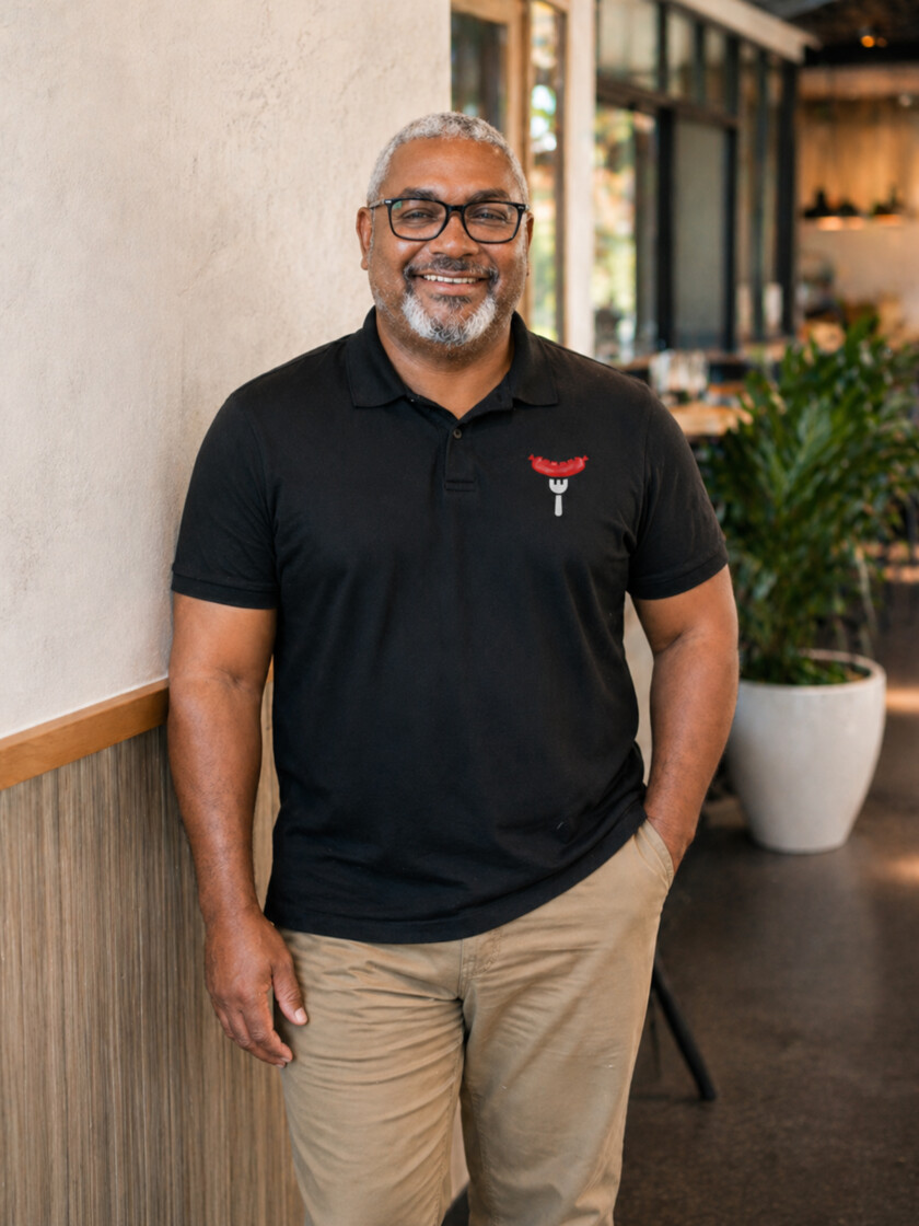 Larry Wilson smiling in a black The Boudin Company polo shirt inside the restaurant